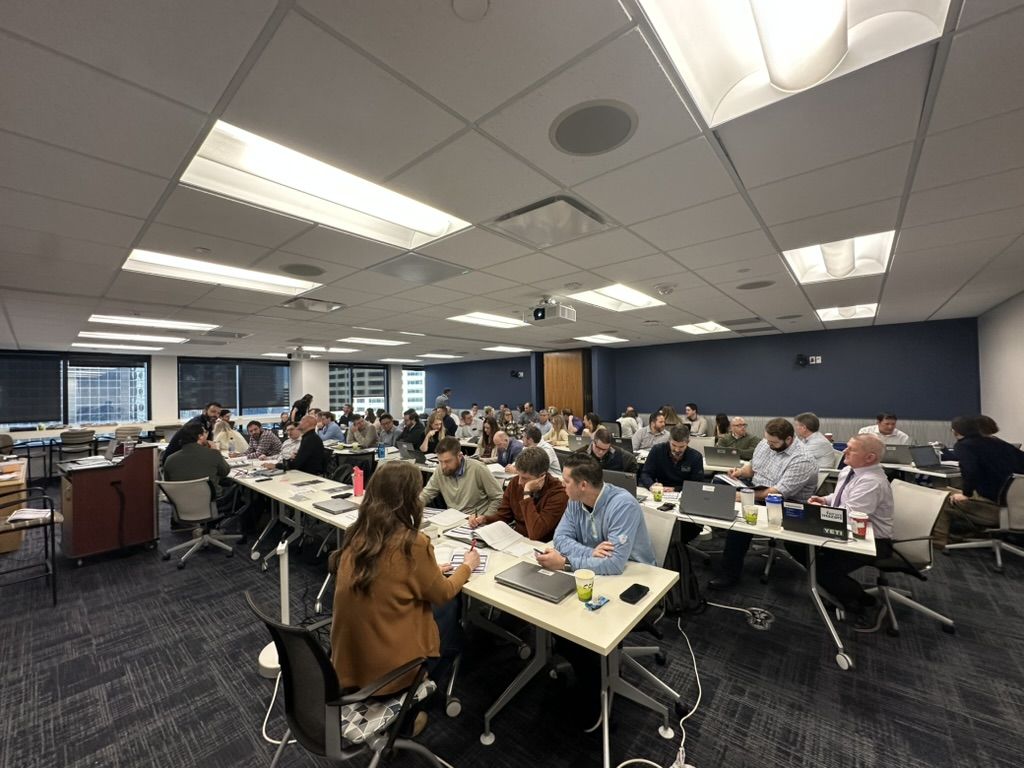 A full room of professionals working on laptops and workbooks during an instructor-led AI workshop